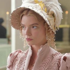 a woman in a pink dress and white hat is looking at the camera while wearing a large, feathered hat