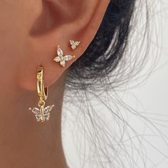 a close up of a person's ear wearing gold earrings with butterflies on them