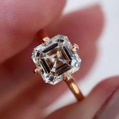 a woman's hand is holding an engagement ring with a fancy diamond in the center