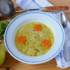 a bowl of soup with carrots and noodles on a table next to an apple