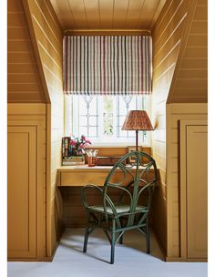 a chair sitting in front of a window next to a desk with a lamp on it