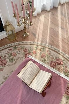 an open book sitting on top of a rug in front of a fireplace with candles