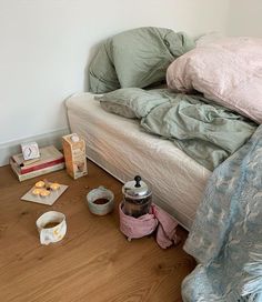 an unmade bed sitting on top of a wooden floor next to pillows and other items