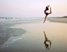 a woman jumping into the air on top of a beach