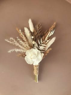 a boutonniere with dried flowers and feathers on a brown plate against a beige background