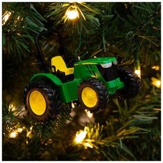 a green tractor ornament hanging from a christmas tree with yellow lights on it