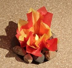 an orange and yellow paper flower sitting on top of some rocks next to a candle