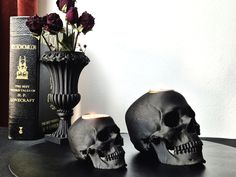 two skulls are sitting on a table next to a book and vase with flowers in it