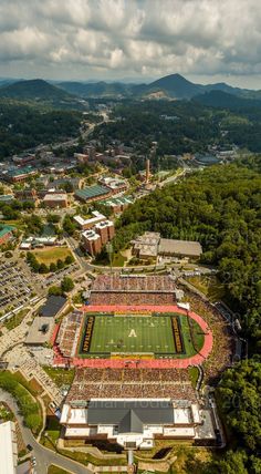 an aerial view of a football field and stadium in the distance with mountains in the background