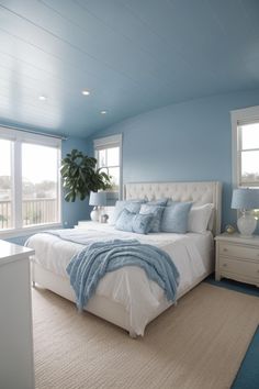 a bedroom with blue walls and white bedding in the center, along with two windows