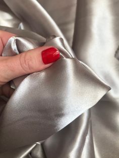 a woman's hand with red nail polish on top of a silver satin fabric