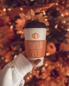 someone holding up a cup of coffee in front of a christmas tree with pumpkins on it