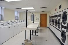 an empty laundry room with washers and dryers in the foreground, next to a long row of washing machines