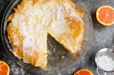 an orange pie with powdered sugar on top sits on a plate next to sliced oranges