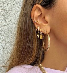 a close up of a person wearing gold ear cuffs and earrings with charms on them