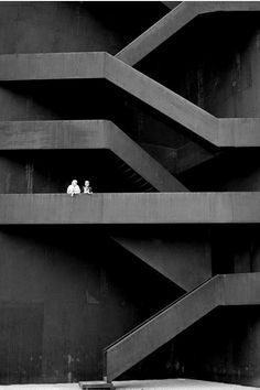 black and white photograph of two people sitting at the top of a staircase in front of an apartment building