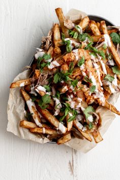 french fries covered in ranch dressing and garnished with cilantro on parchment paper