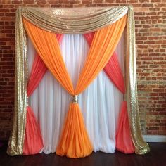 an orange and white drape with gold sequins on the top is set up in front of a brick wall