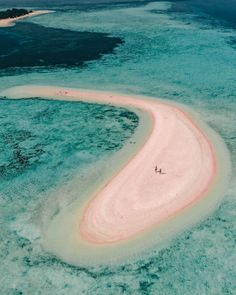 two people are walking on an island in the middle of the ocean with pink sand