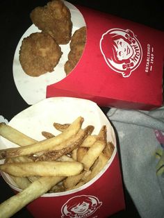 two red boxes filled with fried food on top of a black table next to white plates