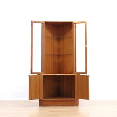 a tall wooden cabinet sitting on top of a hard wood floor next to a white wall