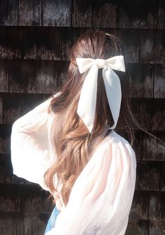 a woman with long hair and a white bow on her head is standing in front of a brick wall