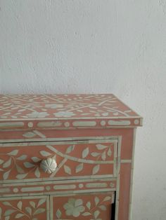 an old pink and white painted dresser with flowers on the front, drawers are closed