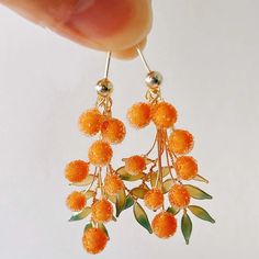 These handcrafted resin orange stud earrings are a vibrant addition to any jewelry collection, inspired by nature's beauty. Each earring features delicate, frosted orange beads, designed to resemble ripe oranges, arranged on golden stems that cascade down gracefully. The beads are accented with tiny green enamel leaves for a natural, organic touch. Lightweight and eye-catching, they are perfect for adding a pop of color to both casual and formal outfits. The earrings are completed with 925 sterling silver stud pins, adding durability and elegance to the design, making them a unique and stylish accessory for any occasion. Orange Frosting, Fruit Jewelry, Orange Earrings, Formal Outfits, Thanksgiving Gift, Unique Jewelry Designs, Fall Jewelry, San Rafael, Jewelry Unique