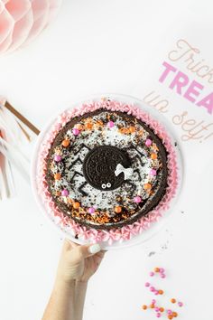 a person holding a cake with sprinkles and oreo cookies on it