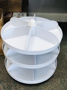 three tiered white cake stand on top of a table with boxes in the background