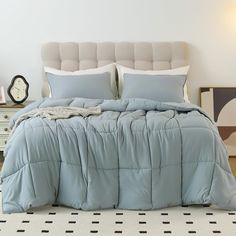 a bed with blue comforter and pillows in a white room next to a clock