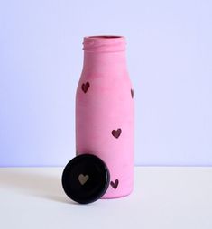 a pink bottle with hearts painted on it and a black lid next to the bottle