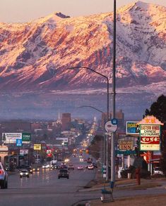 the mountains are covered in snow as cars drive down the street at dusk on a city street