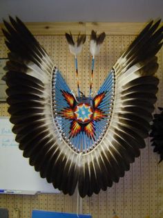 an eagle made out of feathers hanging on a wall next to other art work items