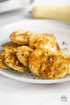 some fried food on a white plate with a banana in the backgroung