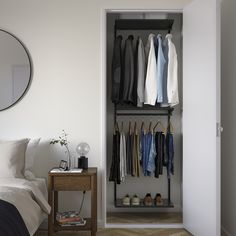 an open closet with clothes and shoes hanging on the wall, next to a bed