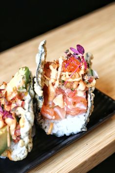 two pieces of sushi are sitting on a black plate with garnishes