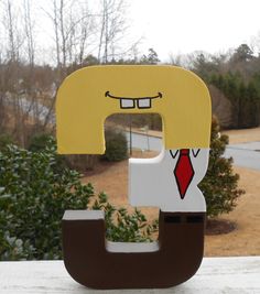 a wooden letter shaped like a man wearing a suit and tie, with trees in the background