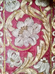 an embroidered fabric with flowers and leaves in gold, pink and white colors on a red background