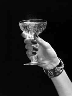 a woman's hand holding a wine glass in black and white with nail polish on it