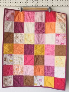 a patchwork quilt hanging on the wall with pegs in front of it,