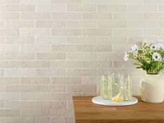 three vases with flowers on a table in front of a white brick wall background