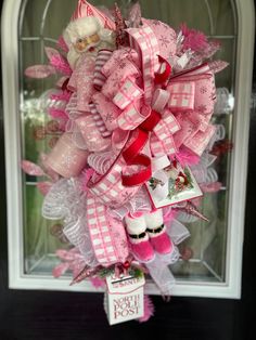 a pink and white christmas wreath hanging on the front door with santa's helper