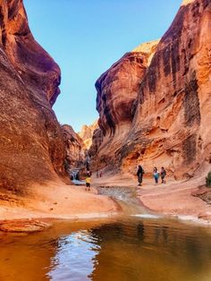 people are walking through the narrow canyons in wading water, with large rocks on either side