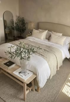 a white bed sitting next to a table with a plant on top of it in a bedroom