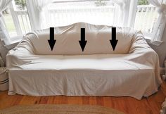 a white couch with three arrows pointing to the right and left ends, in front of a window