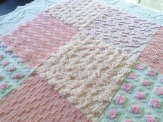 a crocheted blanket with pink and white flowers on it, sitting on top of a table