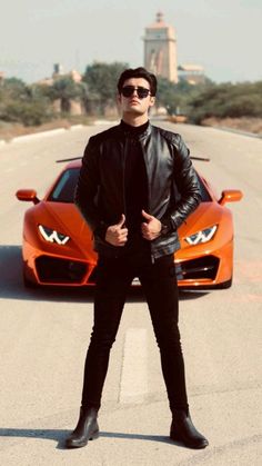 a man standing next to an orange sports car in front of him on the road