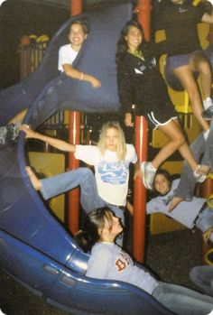 a group of people sitting on top of a blue slide in a play area at a park