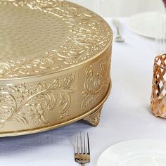 the table is set with gold plates, silverware and an ornately decorated cake